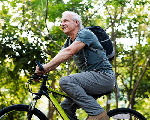 senior man riding his bike with green trees in background planning for retirement