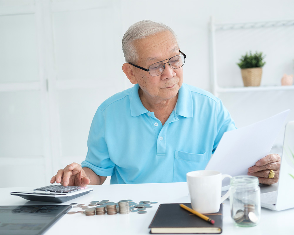 senior man sitting at desk looking at financial paperwork with calculator will i have enough to retire